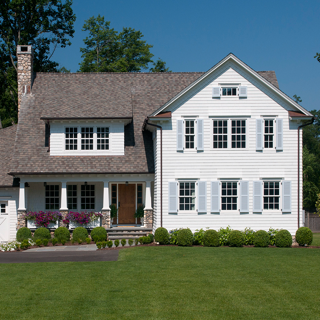 White colonial house with gray roof, white shutters, covered porch with white columns, and two dormer windows.